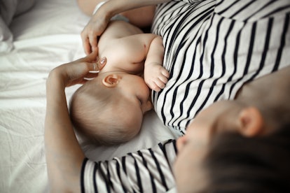 Mom in a striped dress breastfeeds a baby on a white sheet, top view. Concept maternity and breastfe...
