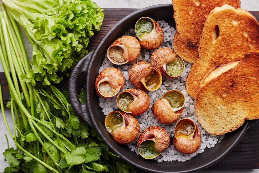 Escargots de Bourgogne - Snails with herbs butter on gray background. Salad