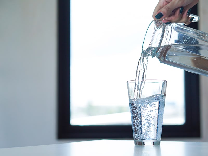 Woman hand holding jar of water and pouring water into a glass.