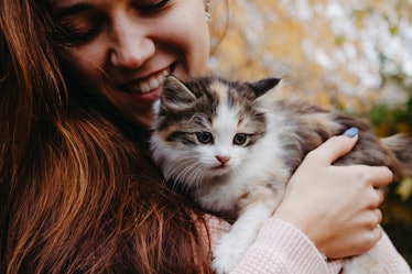 A woman holds a little kitten in her arms and smiles while she looks down.