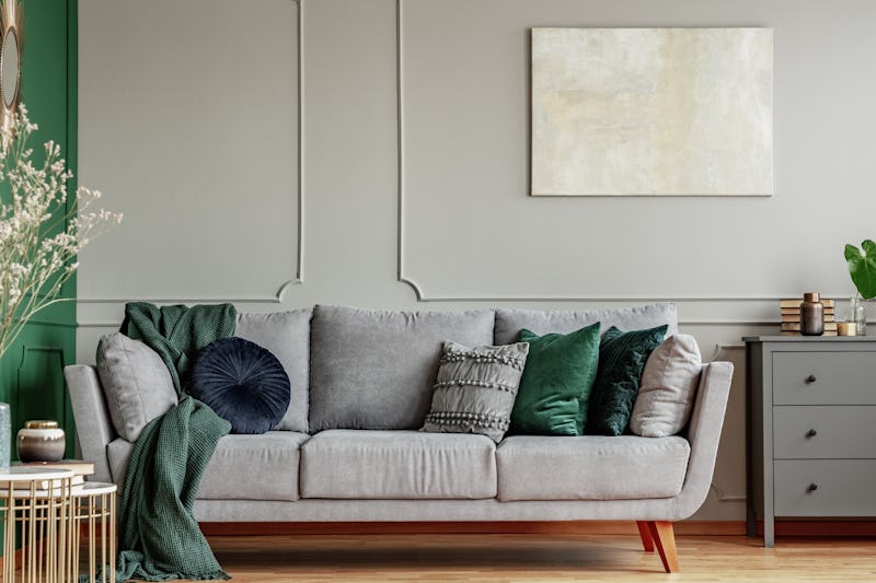 Pillows on long comfortable living room couch in grey scandinavian style interior with wooden floor