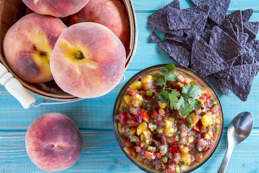 Fresh organic yellow peaches in wooden bushel basket with bowl of homemade peach salsa with spoon an...