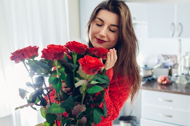 A young woman with red lipstick smells her gorgeous bouquet of roses in her white bedroom.