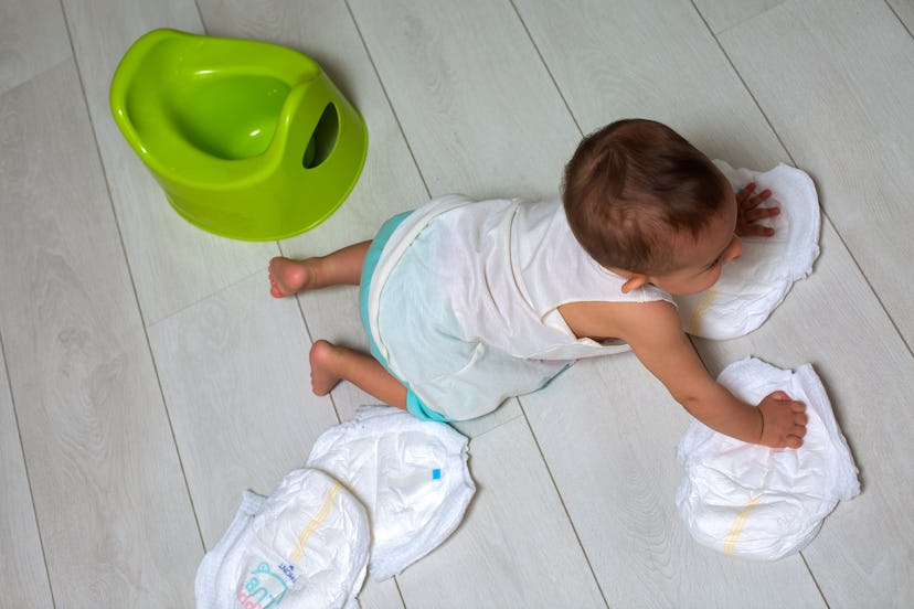 potty training concept. A cute little baby in a room on the bright floor plays with a diaper and an ...