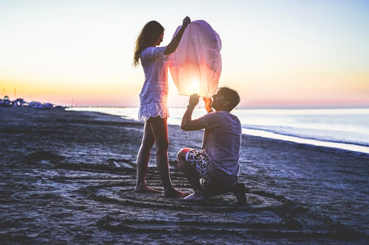 A couple gets a lantern ready on a beach to set off over the water at sunset.