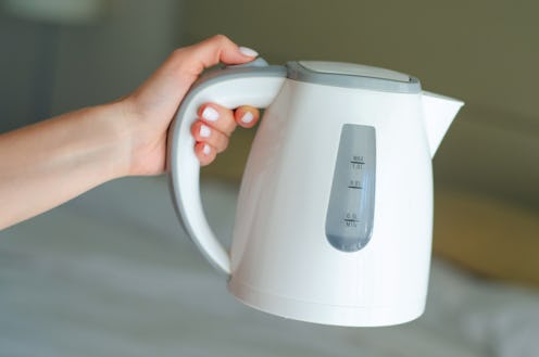 Women hand hold the plastic electric kettle, preparing hot drink, click on the button
