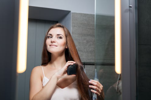 Young woman brushing hair in front of a bathroom mirror