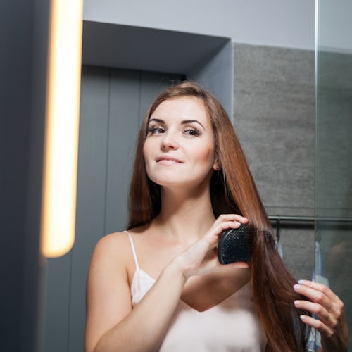 Young woman brushing hair in front of a bathroom mirror