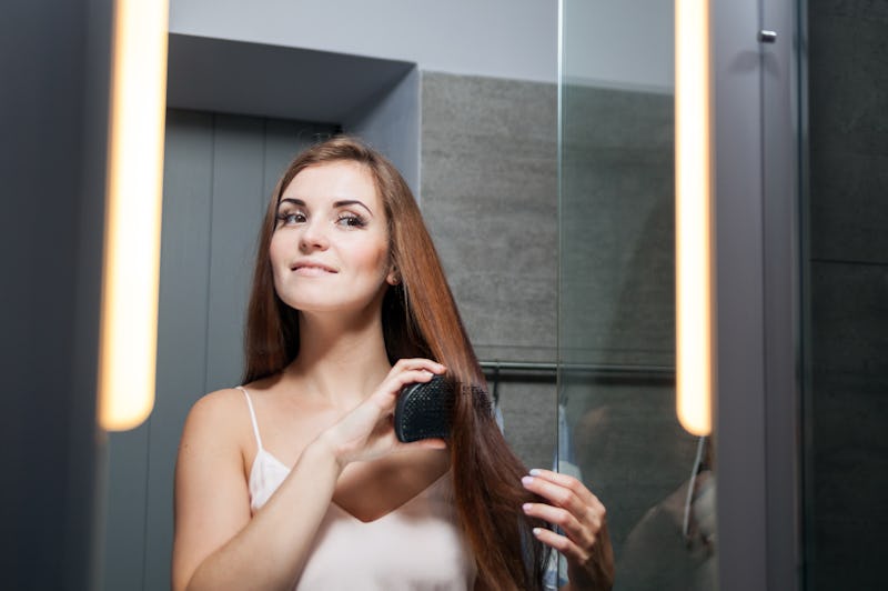 Young woman brushing hair in front of a bathroom mirror