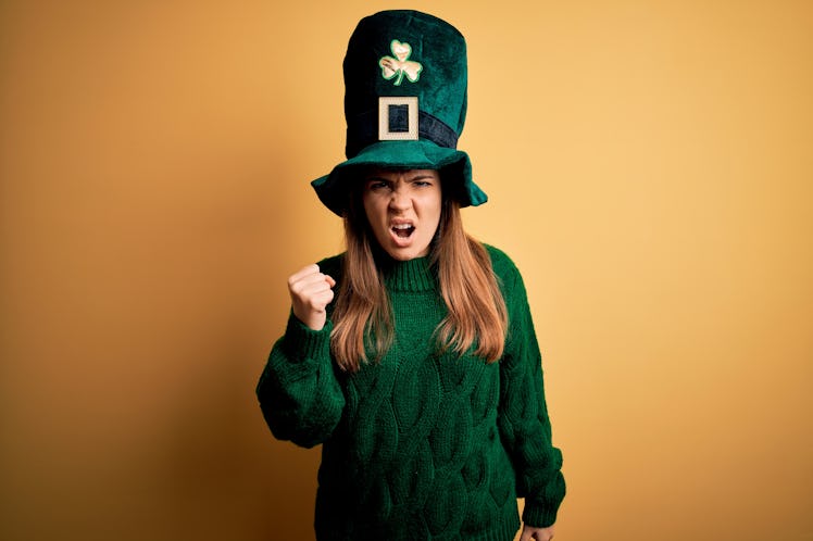 Young beautiful brunette woman wearing green hat on st patricks day celebration angry and mad raisin...