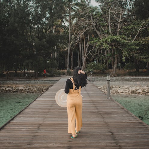 A girl wearing a black and yellow jumpsuit walking away to her solo vacation.