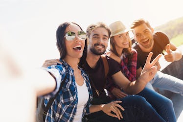 A group of backpackers smile and take a selfie on a sunny day.