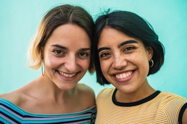 Portrait of lovely lesbian couple having fun and taking a selfie against light blue background. LGBT...
