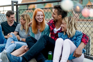 A group of friends laughs while hanging out and enjoying beers on a roof.