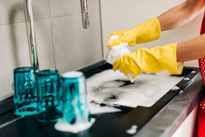 Woman in yellow protective rubber gloves washes dishes in the kitchen.
