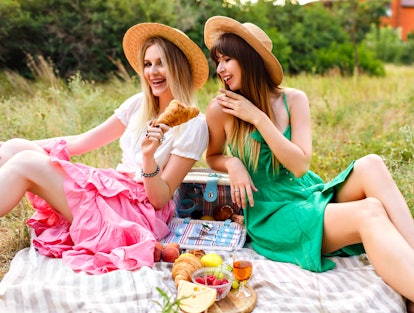 Outdoor countryside portrait of two happy sisters and best friends, enjoying picnic at vintage Frenc...