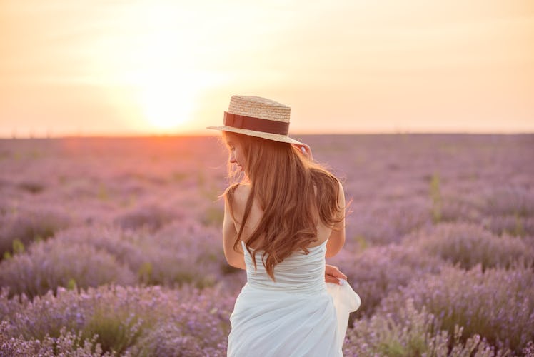 Back view of beautiful girl in a white dress and hat in a lavender field at sunset
