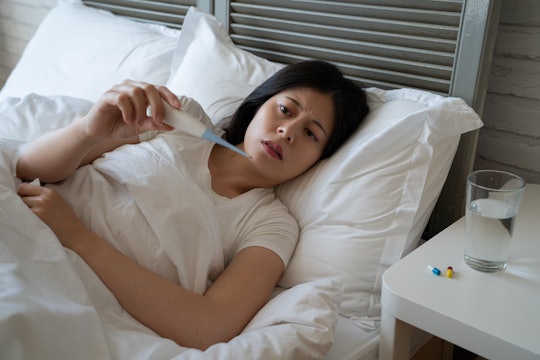 sick asian woman in bed taking temperature