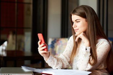 Attractive businesswoman is talking to her manager using FaceTime on her smartphone in the cafeteria...