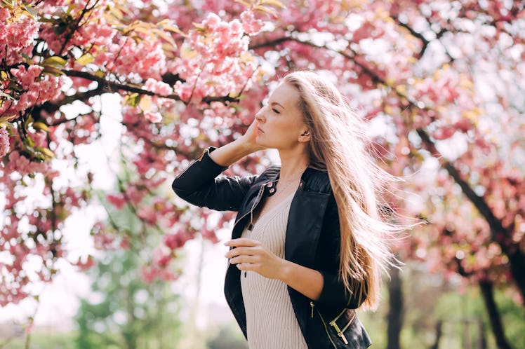 A close-up portrait of a blonde girl against the backdrop of a Japanese flowering tree of sakura. A ...
