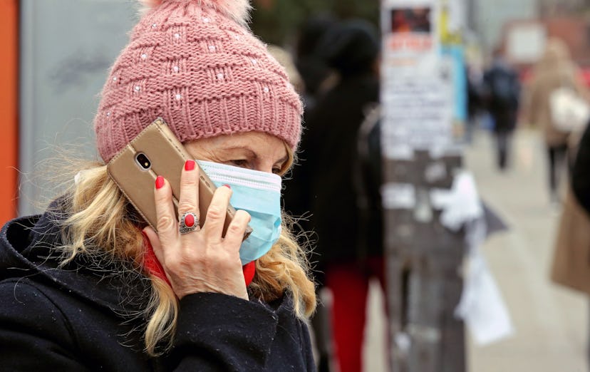 A woman wearing a surgical mask talks on the phone while waiting for a bus at a bus stop in Belgrade...