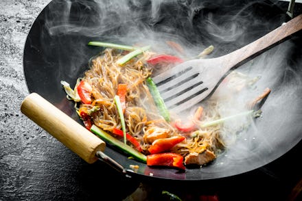 Hot wok Chinese cellophane noodles in a pan with a spatula. On black rustic background