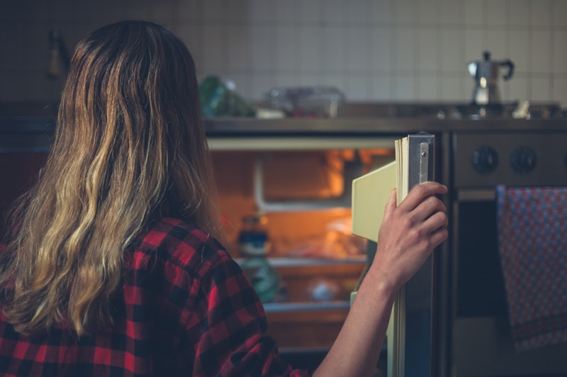A young woman is opening the door of her fridge