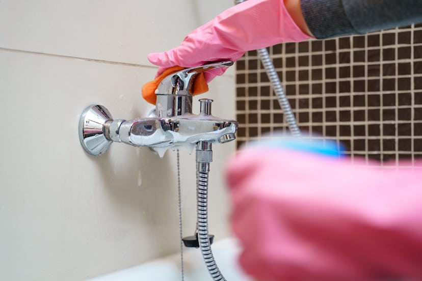 Woman 's hand in rubber gloves with cleaning agent washing bathtub mixer