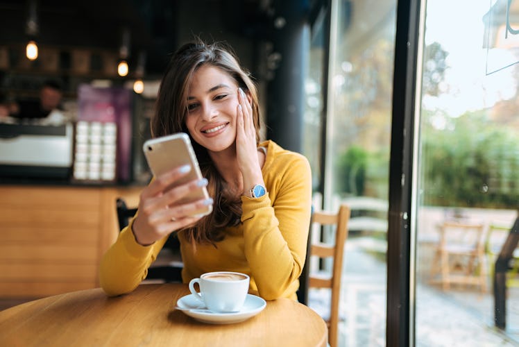 Young smiling woman using smarphone in the cafe. Front view.