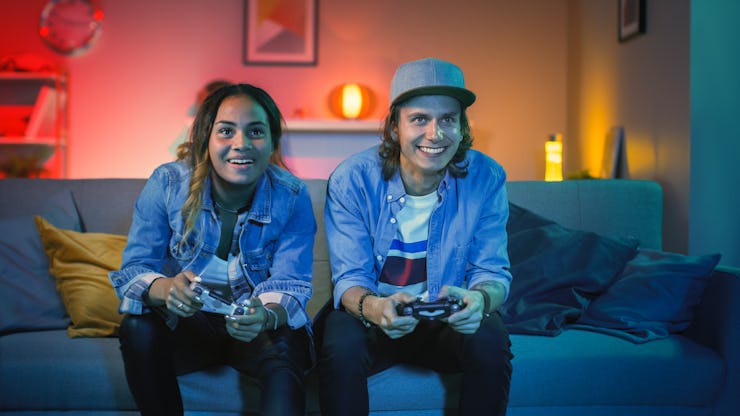 Excited Black Gamer Girl and Young Man Sitting on a Couch and Playing Video Games on Console. They P...