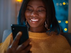 A woman in a yellow sweater holds up her iPhone and smiles.