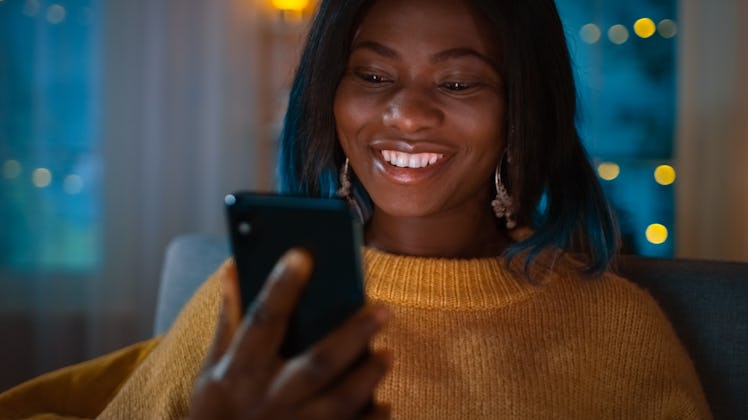 A woman in a yellow sweater holds up her iPhone and smiles.
