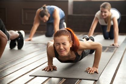 Young fit sporty woman with painful face expression doing hard difficult plank fitness exercise or p...