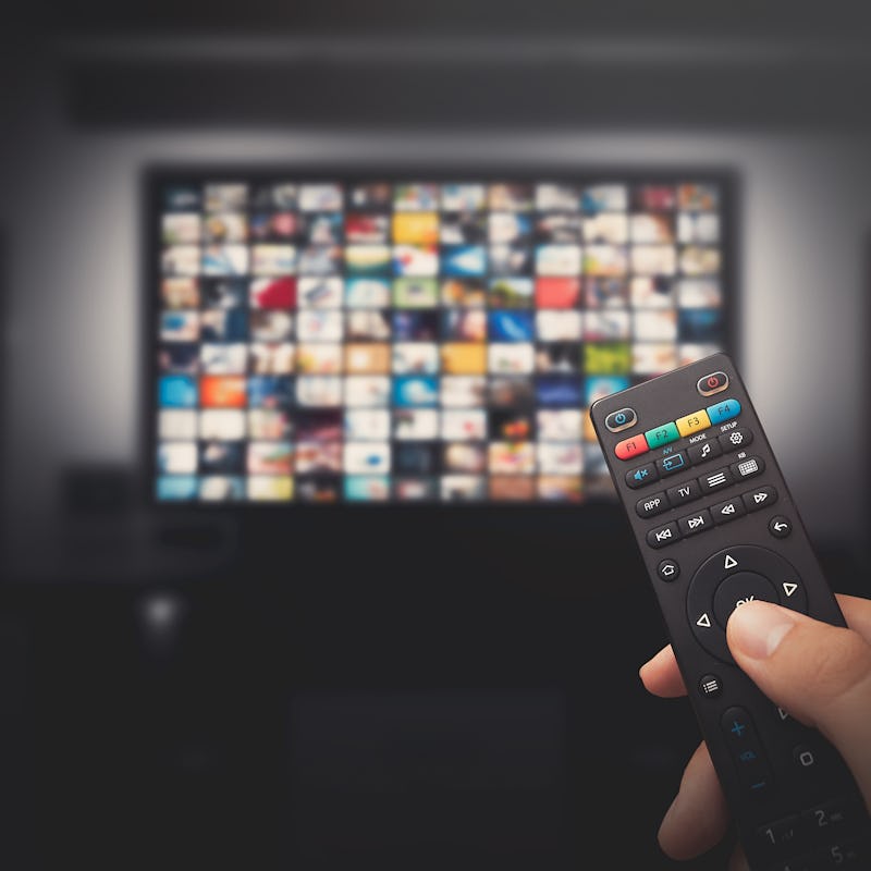 Multimedia video concept on TV set in dark room. Man watching TV with remote control in hand.