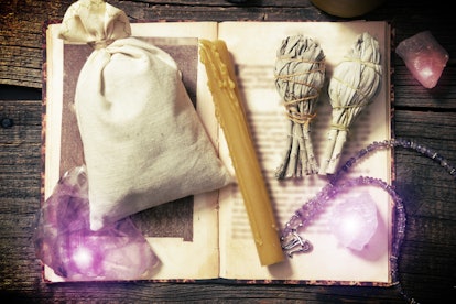 Natural gemstones, white sage, candle, sack on a book on wooden board, witchcraft tools