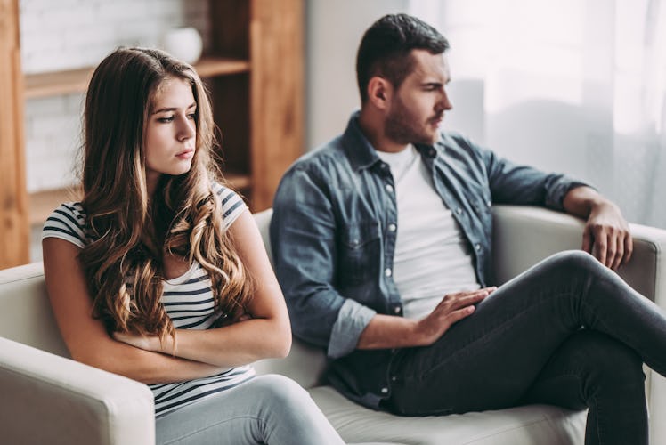 Upset couple at home. Handsome man and beautiful young woman are having quarrel. Sitting on sofa tog...