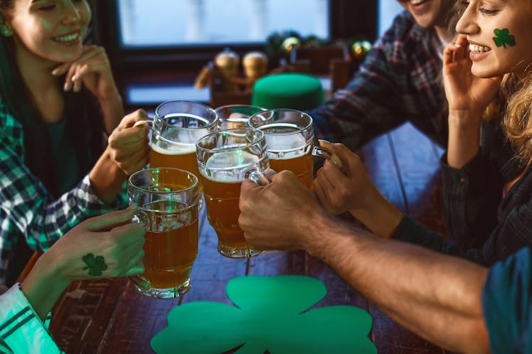 A group of friends dressed up in green for St. Patrick's Day toast their beers at a bar.