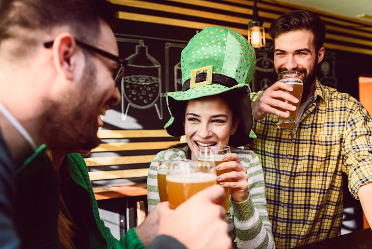 Three friends clink their beers and celebrate St. Patrick's Day at a bar.