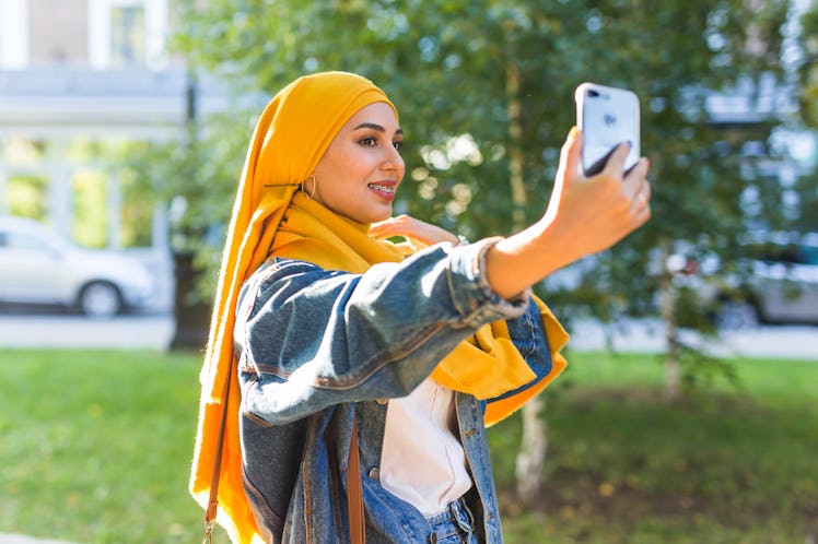 Muslim girl in hijab makes a selfie on the smartphone standing on the street of the city