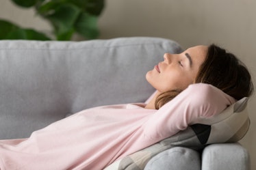 A woman wearing a pink sweater sleeps on a gray couch.