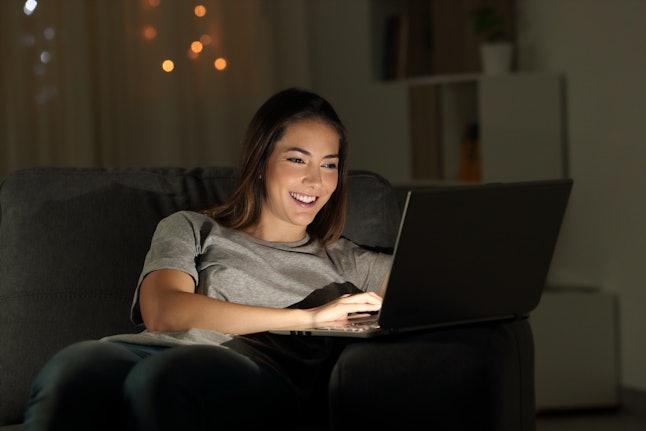 Woman using a laptop in the night sitting on a couch in the living room at home