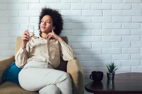 Young beautiful african american woman relaxing at home, drinking wine.