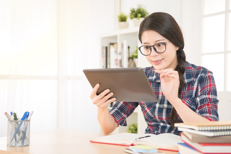 Young beautiful female student using a tablet computer while studying and organizing her time. mixed...