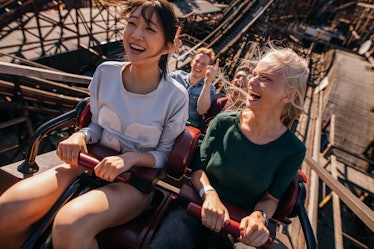 Two friends on a roller coaster laugh and smile right while going up a hill.