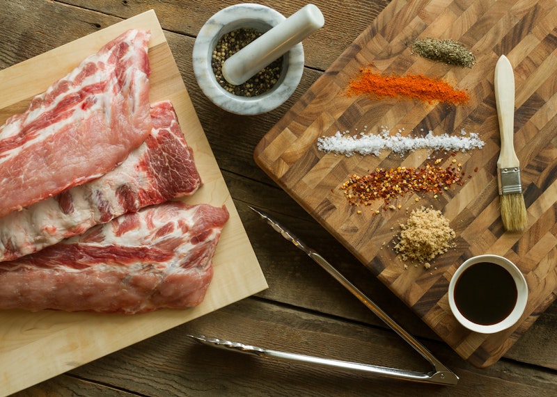 Horizontal photo of a three full rack of Raw Ribs with mortar and pestle, bbq sauce Baste, Herbs and...