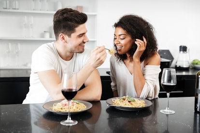 Beautiful young multiethnic couple having a romantic dinner at home, drinking red wine and eating pa...