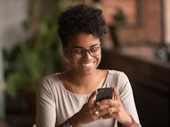 Happy millennial african american woman holding smartphone using ecommerce apps, playing mobile game...