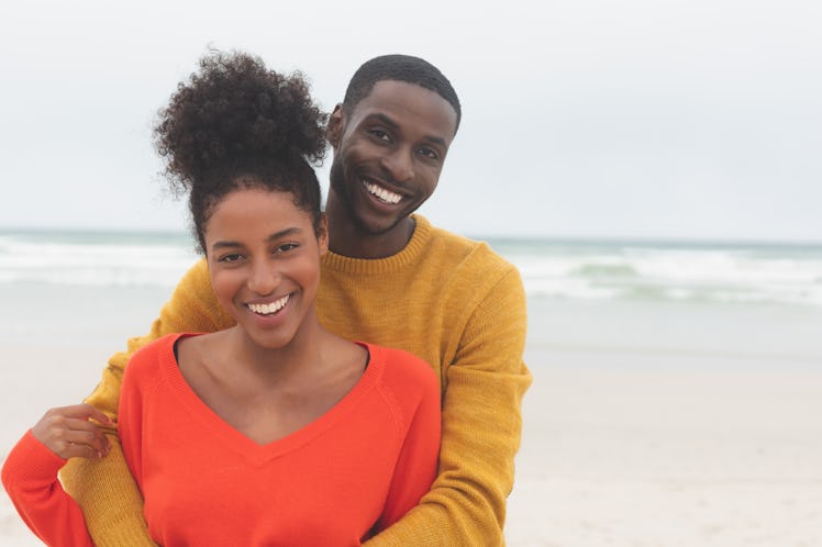 Portrait of diverse couple standing at beach on a sunny day. They are smiling and looking at camera