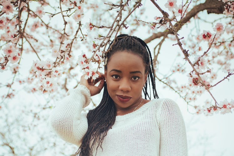 A woman in a white sweater stands next to some cherry blossoms outside on a tree.