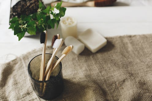 eco natural bamboo toothbrushes in glass on rustic background with greenery. sustainable lifestyle c...